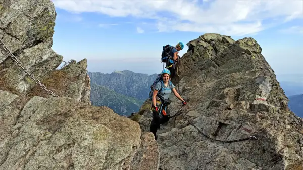 Dwoje turystów wspina się po skalistych tatry wysokie szlaki, korzystając z łańcuchów. Widok na góry i błękitne niebo.