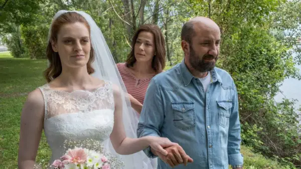 Sposa con velo e bouquet, accompagnata da un uomo in camicia di jeans e una donna sullo sfondo. Scena del **cento domeniche finale**.