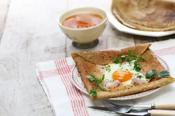 Crêpe de sarrasin garnie d'un œuf au plat, de jambon et d'herbes fraîches, servie avec une compote.