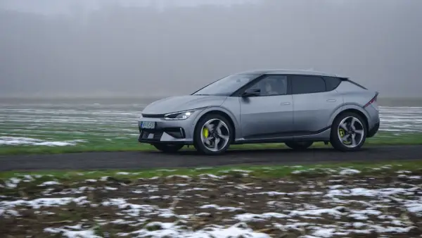 Srebrna Kia EV6 jedzie po drodze, otoczona polami z resztkami śniegu.