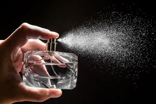 Dłoń trzyma szklaną butelkę, z której rozpyla się mgiełka. Czy to woda toaletowa czy perfumowana?