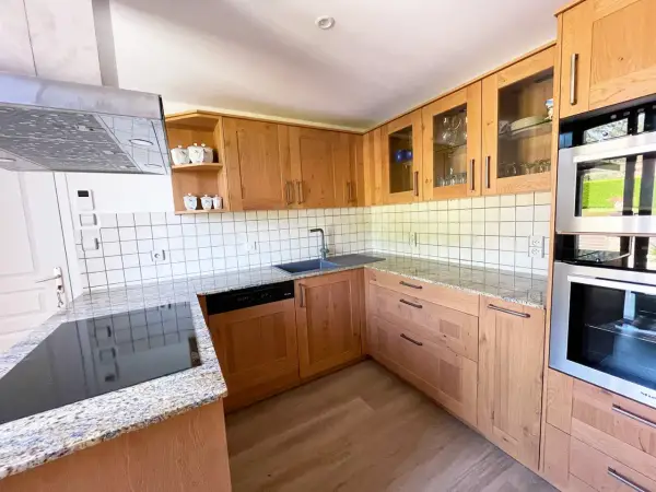 Cuisine en bois clair, avec des placards vitrés rappelant l'intérieur d'un voilier. Le plan de travail en granit et les appareils modernes complètent ce décor chaleureux.