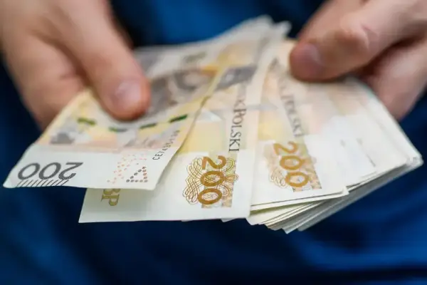 Dłonie trzymają stos banknotów 200 zł. Pieniądze mogą posłużyć do zapłaty czynszu administracyjnego.