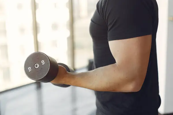 Mężczyzna wykonuje ćwiczenia na biceps z hantlem 10 kg. To jedne z najlepszych ćwiczeń na biceps.