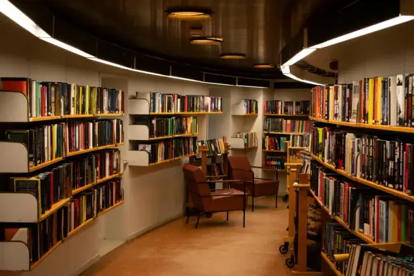 Wnętrze biblioteki z regałami pełnymi książek. Wygodne fotele zapraszają do lektury, a każdy tom czeka na swojego bibliotekarza.