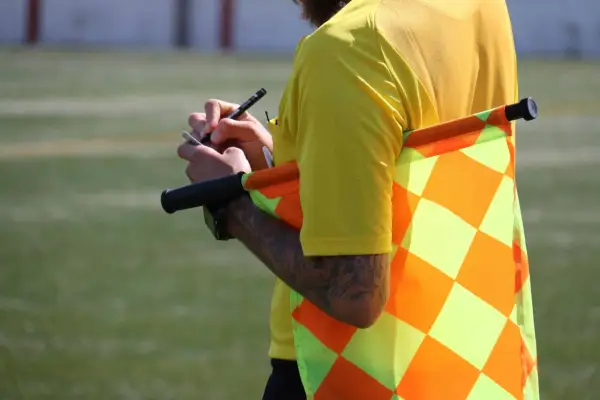 Sędzia piłkarski w żółtej koszulce z chorągiewką i notatnikiem. To akcesoria które posiadają sędziowie piłki nożnej.