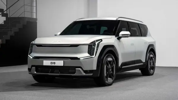 Biały, futurystyczny SUV Kia EV9 z charakterystycznymi światłami LED i masywnymi felgami stoi na szarym tle.