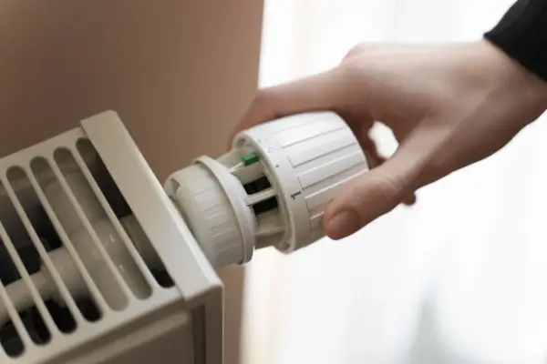 Hand dreht Thermostat einer Heizung. Energie sparen für die Gasheizung 2026.