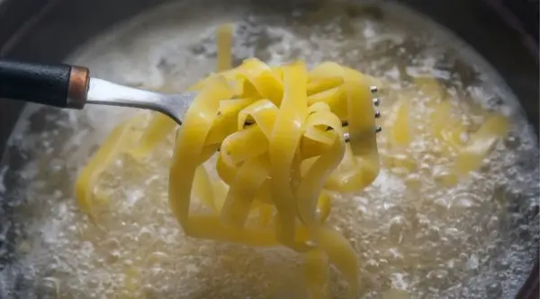 Tagliatelle na widelcu unoszone z wrzącej wody. Prosty sposób, jak ugotować makaron idealnie al dente.