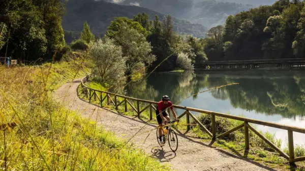 Ciclista pedalea por una de las vías verdes España, junto a un lago sereno y rodeado de exuberante vegetación.
