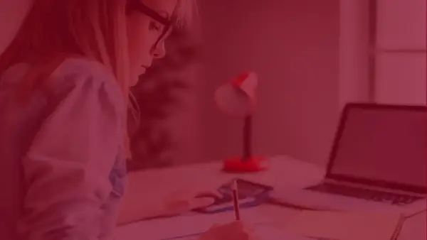 Kobieta z zeszytem i kalkulatorem zastanawia się, ile kosztują studia zaoczne. Obok leży laptop.