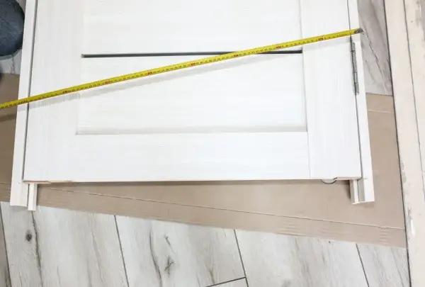 Białe drzwi z widoczną miarką. Mierzone skrzydło drzwiowe ma szerokość ok. 70 cm, co sugeruje jaki otwór na drzwi 70 będzie potrzebny.
