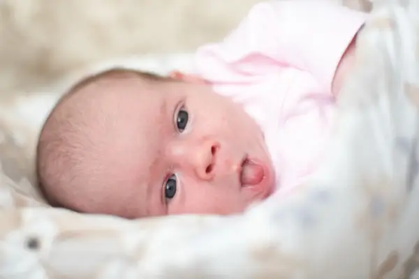 Neonato con lingua bianca, vestito di rosa, guarda incuriosito.