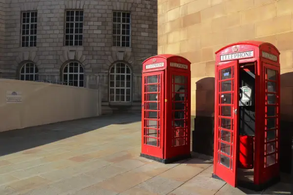 Klasyczne czerwone budki telefoniczne na brukowanym placu, w tle kamienna fasada budynku. Manchester miasto.