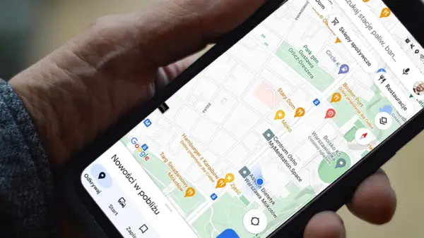 Dłoń trzyma telefon z mapą. Aplikacja do udostępniania lokalizacji pokazuje pobliskie restauracje i sklepy.