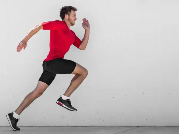 Ein Mann in rotem Shirt und schwarzen Shorts läuft mit hoher Kadenz gegen eine Betonwand.