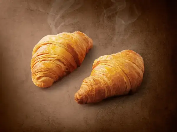 Dwa złociste, parujące croissanty na brązowym tle. Pyszne, choć warto pamiętać o ich kaloryczności.