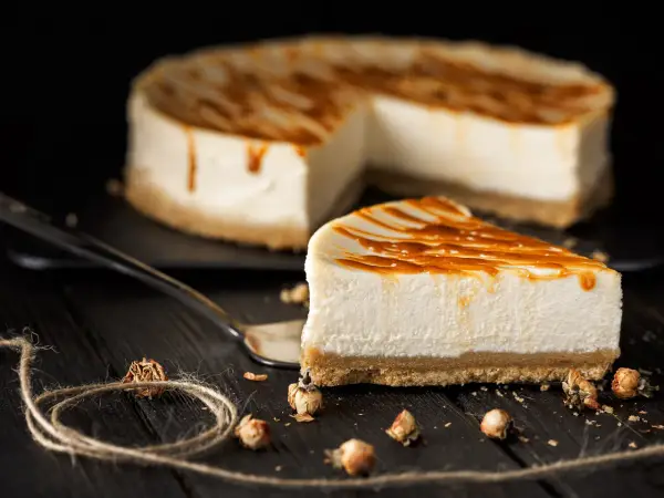 Una fetta di cheesecake fredda senza gelatina, con glassa al caramello, su un piatto scuro.