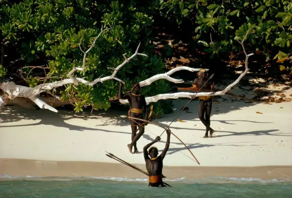 Trzech mężczyzn z plemienia Sentinelese, uzbrojonych w łuki i strzały, stoi na plaży. Sentinel Island, ich dom, chroni ich przed światem.