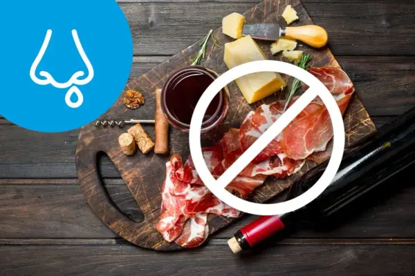 Deska serów i wędlin z winem, z symbolem zakazu. Wskazuje na dietę antyhistaminową, unikającą pewnych produktów.