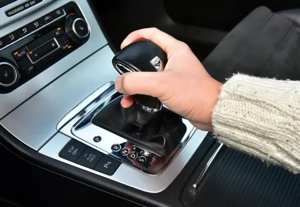 Dłoń trzyma gałkę zmiany biegów w samochodzie. Widoczna jest automatyczna skrzynia biegów DSG z przyciskami ESP, Auto Hold i czujnikami parkowania.