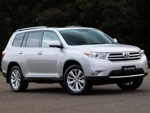 Srebrny Toyota Kluger zaparkowany na drodze, z ciemnym tłem drzew.