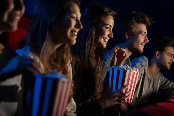 Uśmiechnięci ludzie jedzą popcorn w kinie. Idealny strój do kina to coś wygodnego, jak na przykład bluza.