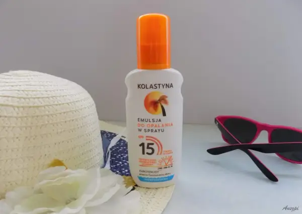 Emulsja do opalania w sprayu Kolastyna SPF 15 z karotenoidami, wodoodporna. Obok kapelusz i okulary przeciwsłoneczne.