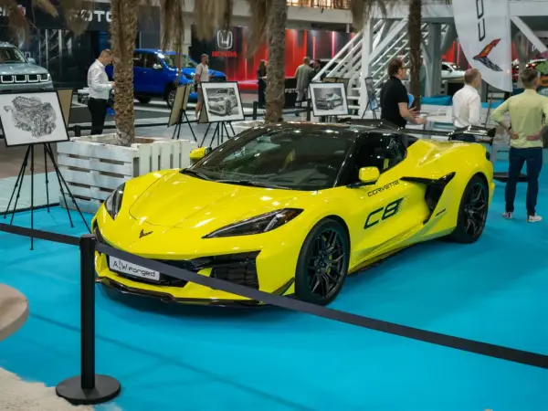 Jaskrawożółty Chevrolet Corvette C8 z czarnym dachem i felgami, prezentowany na niebieskiej podłodze wystawowej.