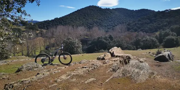 Bicicleta de montaña lista para explorar las **rutas en bici de montaña** en un paisaje rocoso y boscoso bajo un cielo azul.