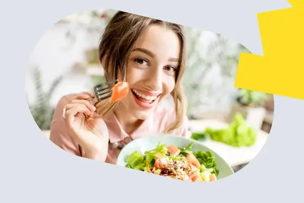 Uśmiechnięta kobieta je sałatkę z łososiem, zastanawiając się, ile omega 3 dziennie jest optymalne.