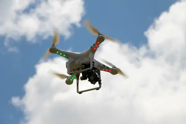 Weiße Drohne mit roten und grünen Lichtern fliegt im blauen Himmel mit Wolken. Beachten Sie die Drohnen Richtlinien für sicheren Flug.
