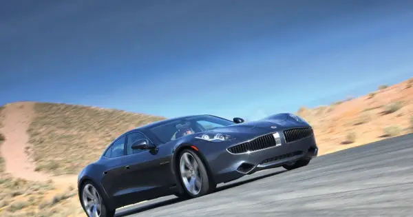 Elegancki, ciemnoszary Fisker Karma sunie po pustynnej drodze pod błękitnym niebem.