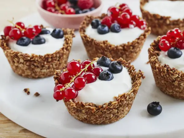Leckere Granola Cups gefüllt mit Joghurt und garniert mit roten Johannisbeeren und Blaubeeren.