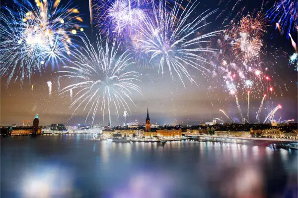 Fyrverkerier lyser upp himlen över Stockholm vid nyår. Vatten reflekterar ljusen från staden och fyrverkerierna.