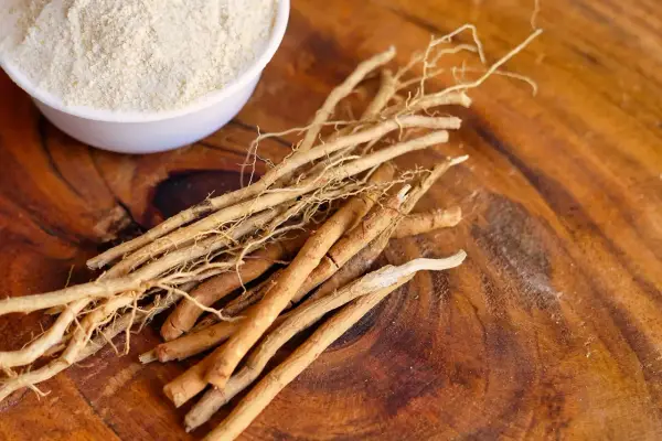 Ashwagandha-Wurzeln und Pulver auf Holz. Mögliche Ashwagandha Nebenwirkungen Haut sind selten, aber bei Einnahme zu beachten.
