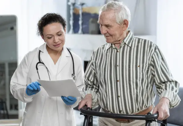 Medico spiega a paziente anziano con deambulatore il significato di un problema cognitivo, mostrando un documento.