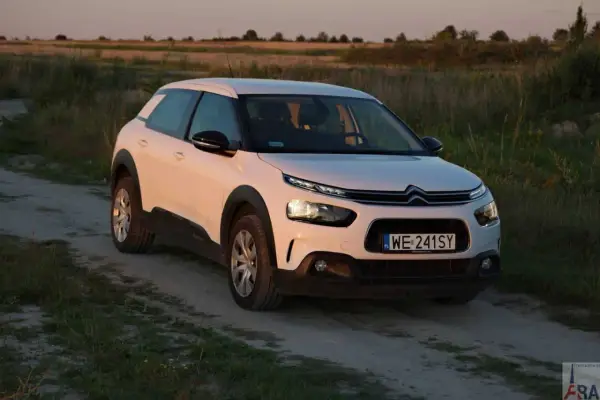 Biały Citroen Cactus na polnej drodze, w tle pole i zachodzące słońce.