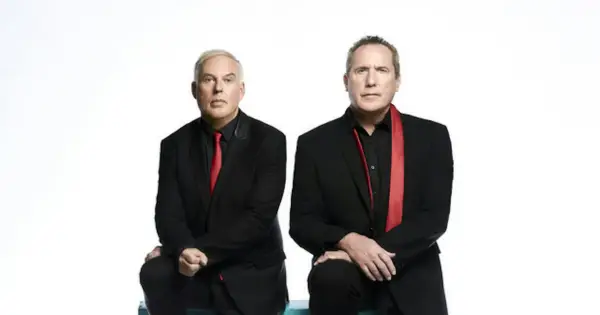 Andy McCluskey i Paul Humphreys z OMD, duet znany z niezapomnianych piosenek, w czarnych garniturach i czerwonych akcentach.
