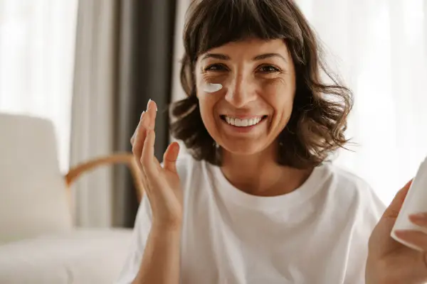 Mujer sonriente aplicándose crema en la mejilla, como si fueran vitaminas para el sol.