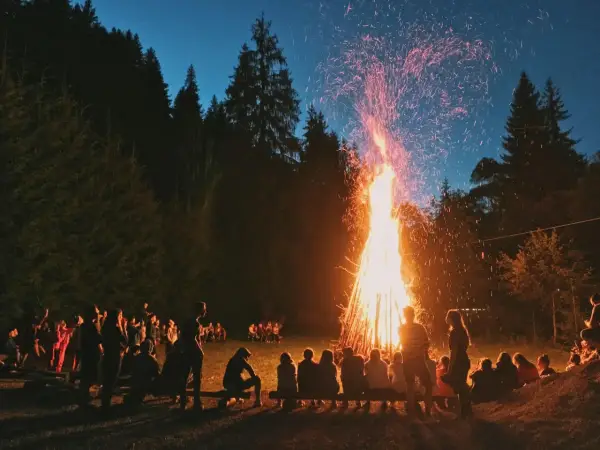 Människor samlas runt en stor brasa i skogen, en vacker svensk tradition som lyser upp natten med gnistor och värme.