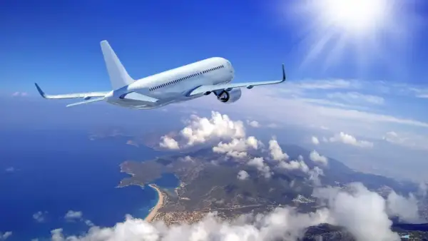 Un aereo bianco solca il cielo azzurro sopra una costa frastagliata. Il sole splende, creando un senso di distacco del vitreo e aereo.