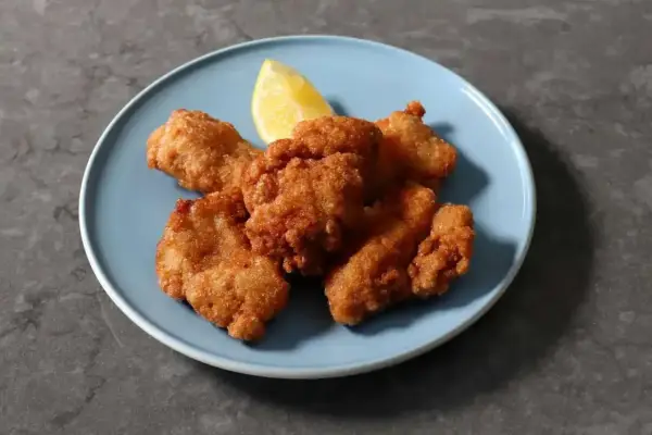 Chrupiący kurczak karaage na niebieskim talerzu, z kawałkiem cytryny.