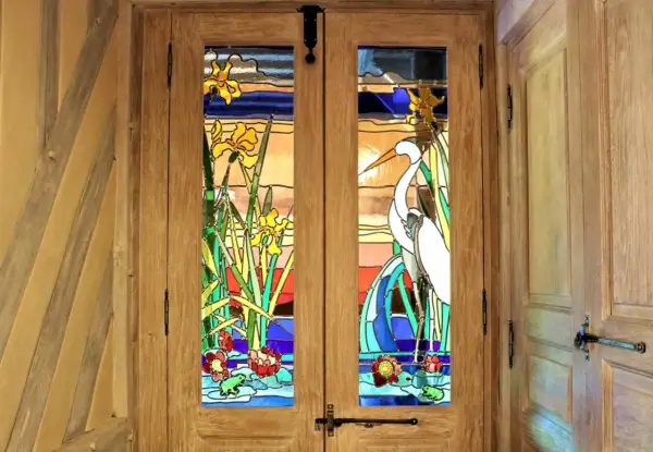 Portes en bois ornées de vitraux représentant des iris, un héron et des nénuphars. L'art de faire des vitraux sublime cette entrée.