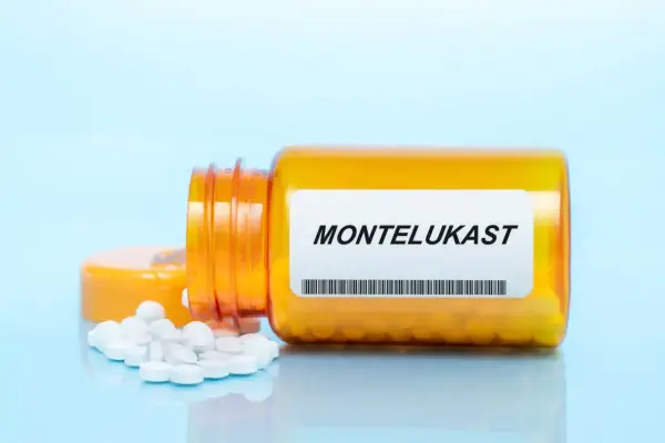 Pomarańczowa butelka z tabletkami montelukast, kilka białych tabletek rozsypanych obok.