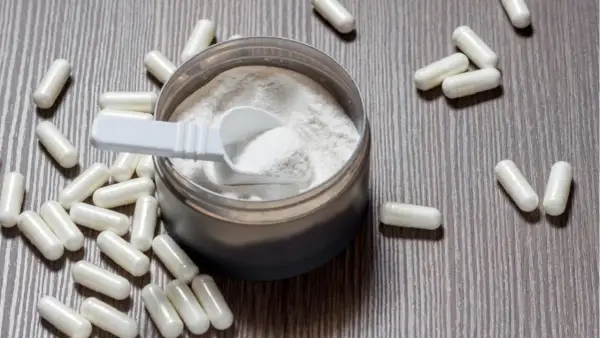 Cápsulas y polvo blanco sobre fondo de madera. Descubre para qué sirve la L-arginina y sus beneficios.
