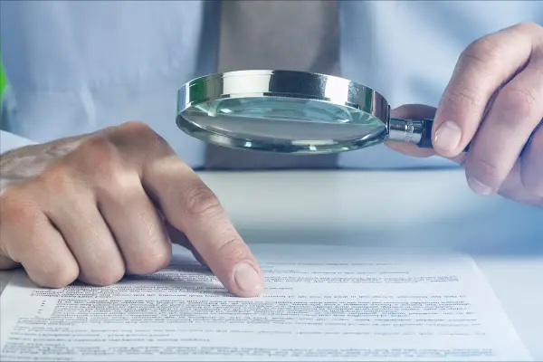Manos examinando un documento con lupa. Se investiga qué es fein, buscando detalles en el texto.