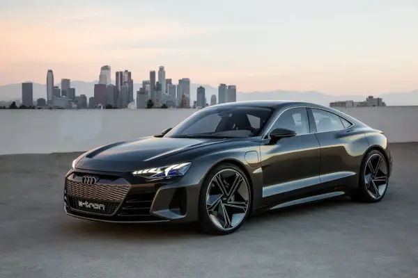 Ciemnoszary Audi e-tron GT stoi na tle panoramy miasta o zachodzie słońca.