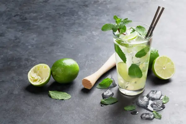 Orzeźwiający **mojito** z limonką i miętą, obok świeże limonki i kostki lodu.