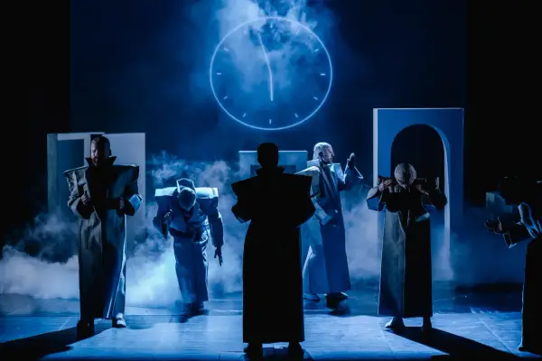 Postacie w futurystycznych strojach na scenie Teatru Arlekin w Łodzi. W tle świecący zegar.